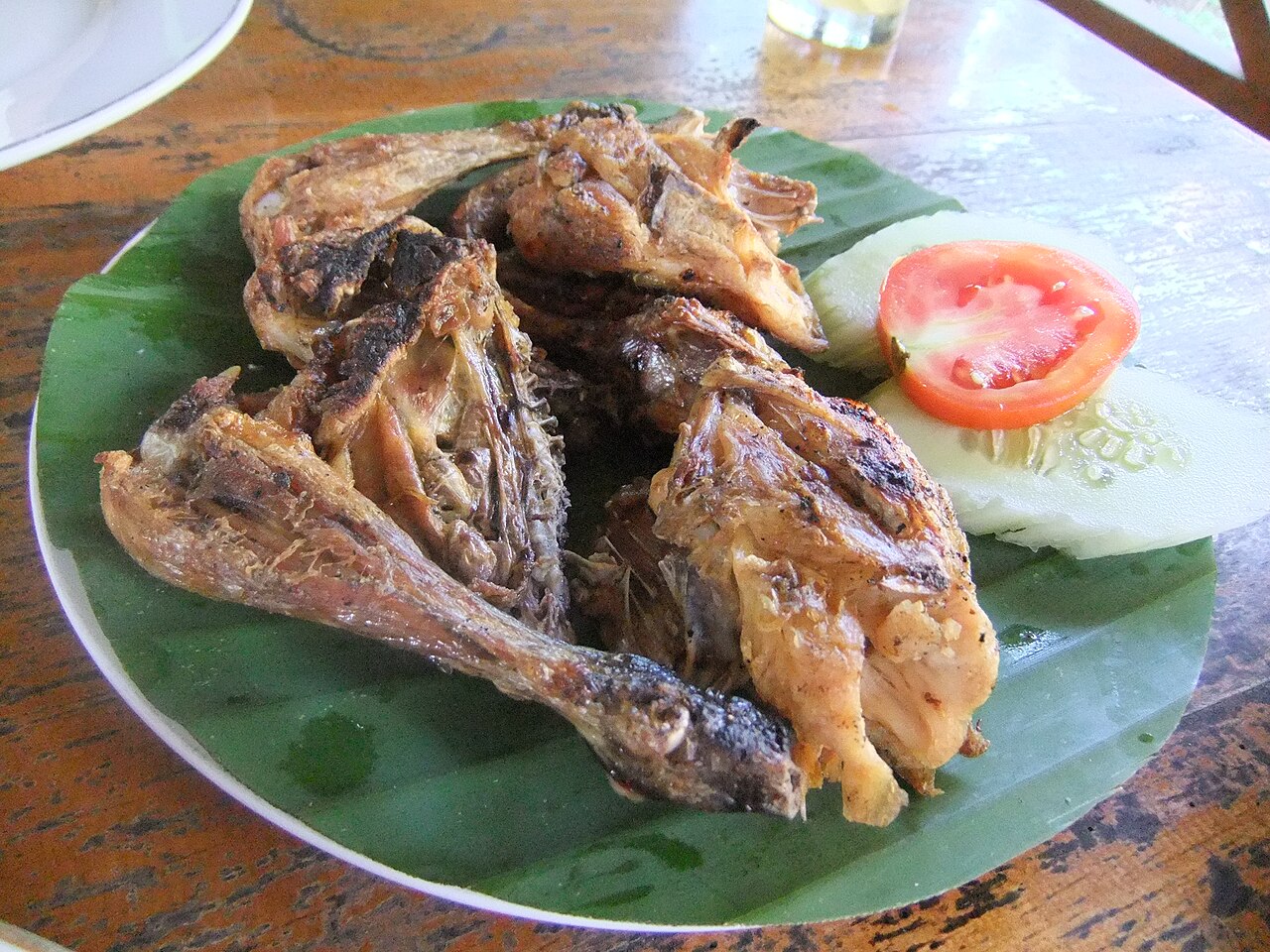 Gegrilltes Ayam-Taliwang-Hühnchen auf Bananenblatt mit Tomaten- und Gurkenscheiben