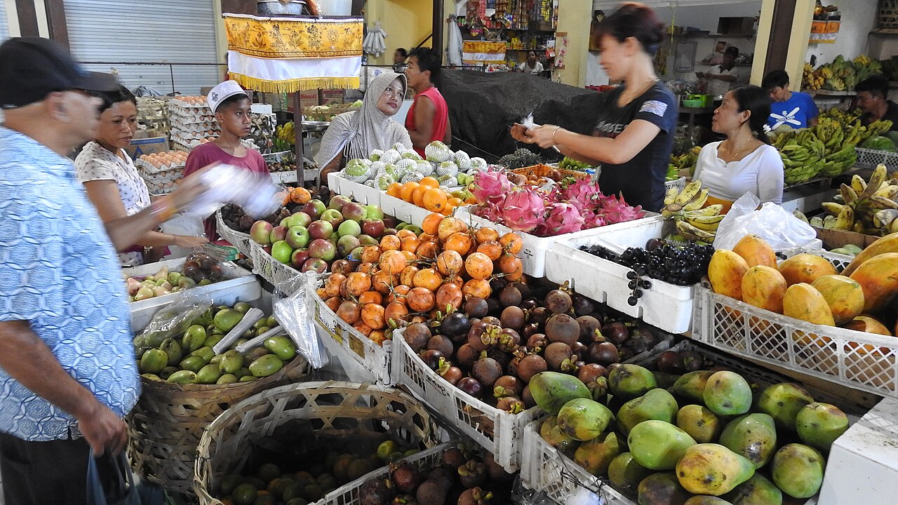 Balinesischer Markt mit Verkäuferinnen und Kunden vor Ständen mit frischem Obst und Waren
