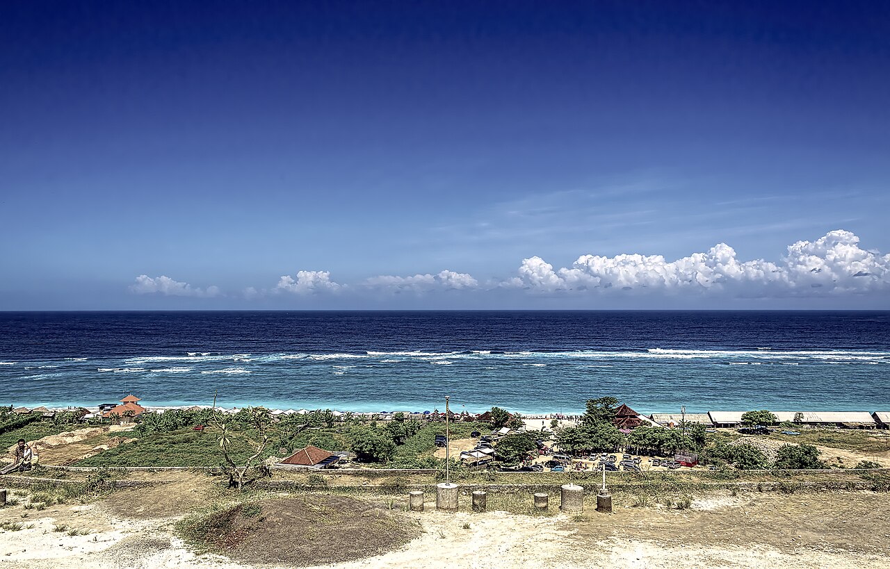 Küstenabschnitt in Bali mit Gebäuden nahe dem Strand, türkisfarbenem Meer und Wellen am Riff