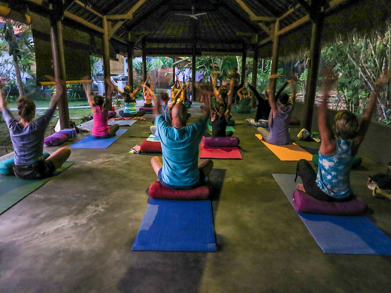 Gruppe bei einer Yoga-Stunde in einem offenen Pavillon, Ansicht von hinten mit bunten Matten