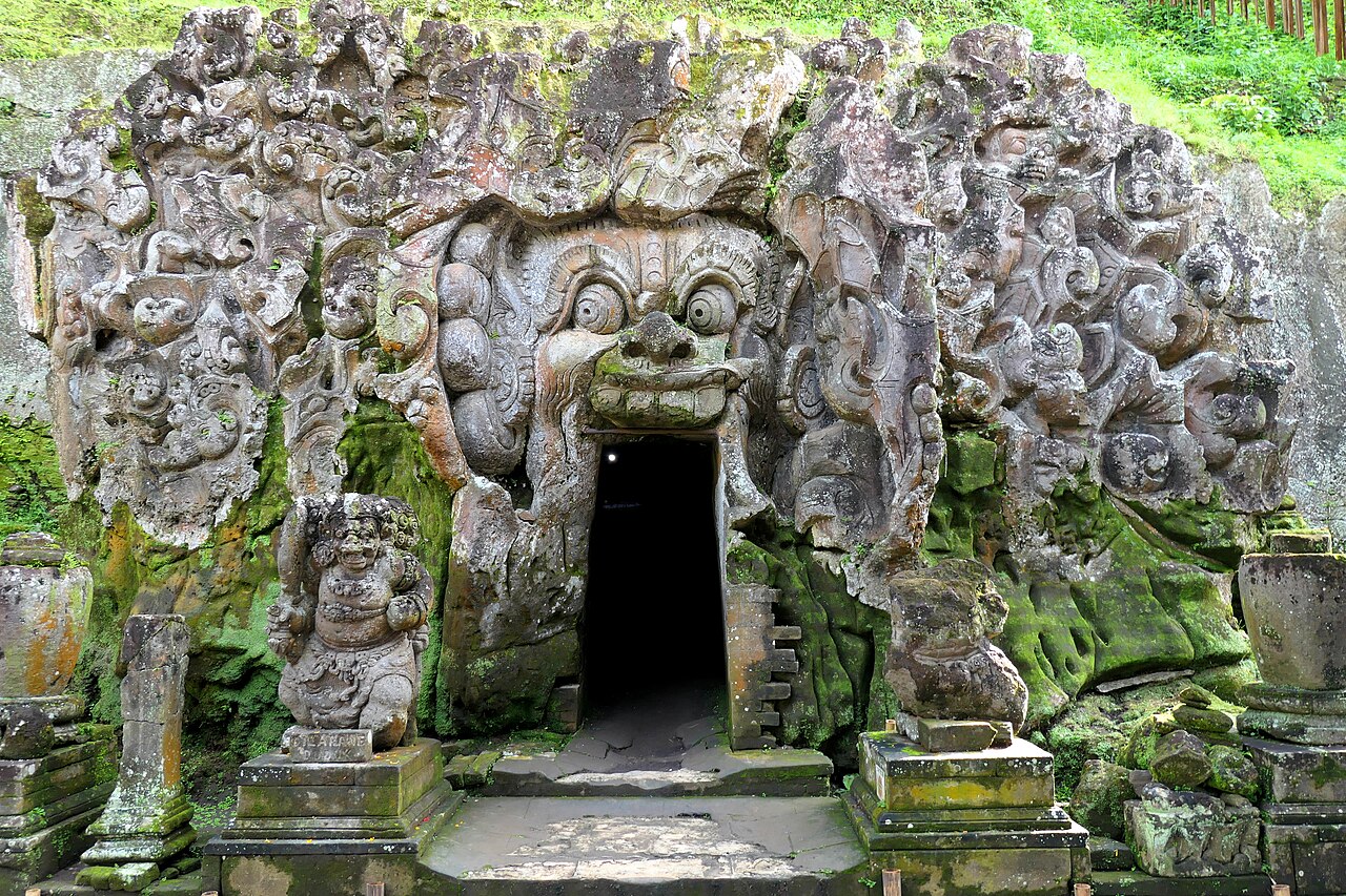 Höhleneingang von Goa Gajah als offener Mund einer steinernen Fratze, ringsum Reliefs und Wächterfiguren