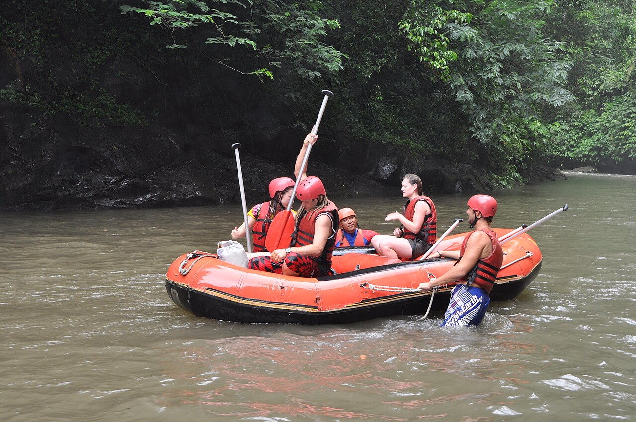 Orangefarbenes Schlauchboot mit Raftern in Helmen und Schwimmwesten auf dem Ayung-Fluss