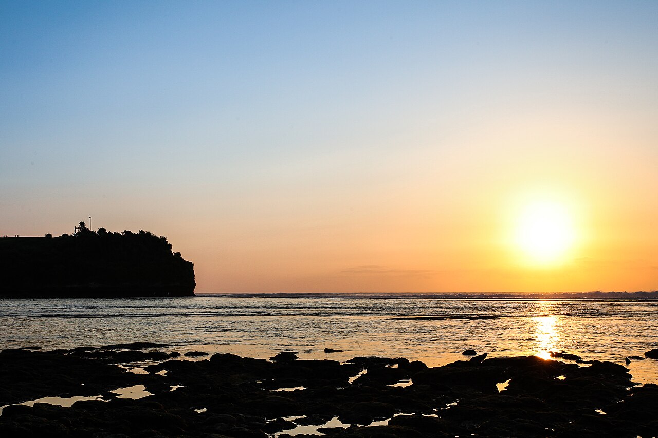 Tiefstehende Sonne über dem Meer am Balangan Beach, Klippe als Silhouette, Riffplatte im Vordergrund