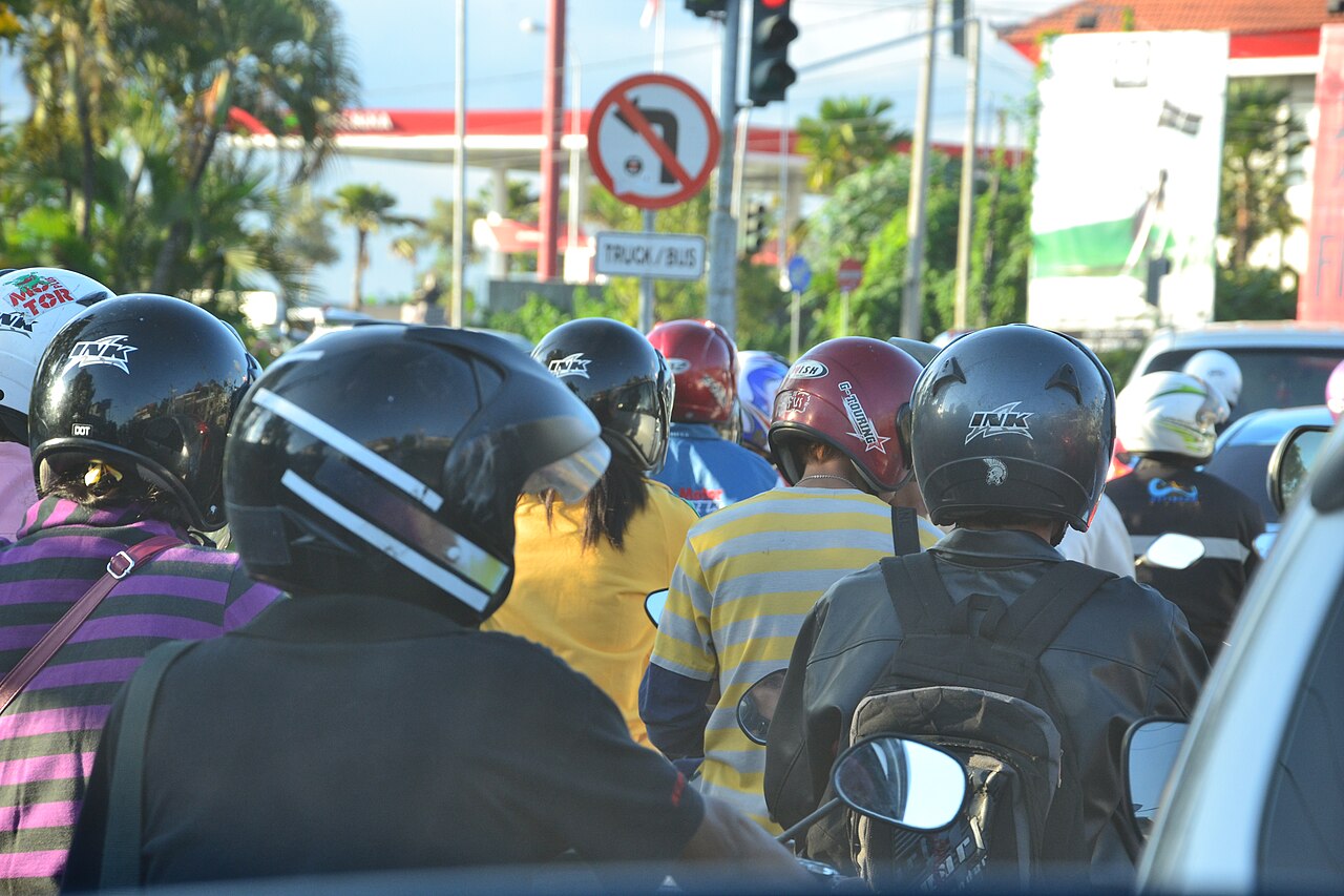 Stau aus Motorrollern mit Helm tragenden Fahrern an einer Ampel auf Bali, Ansicht von hinten
