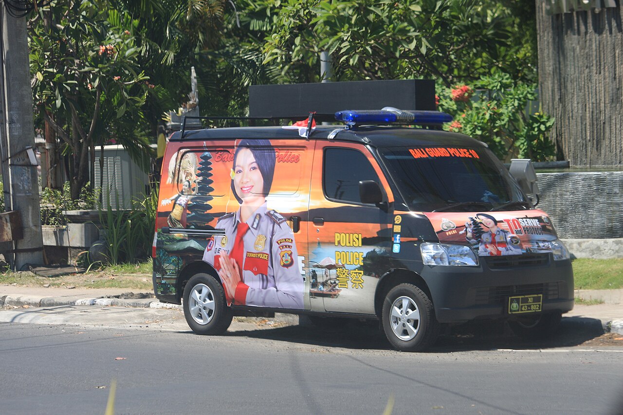 Polizeitransporter mit Blaulicht und bunter Folierung am Straßenrand auf Bali