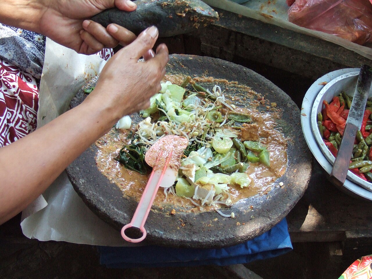 Hände mischen Gemüse, Sprossen und Erdnusssauce in einem Steinmörser für Gado-Gado
