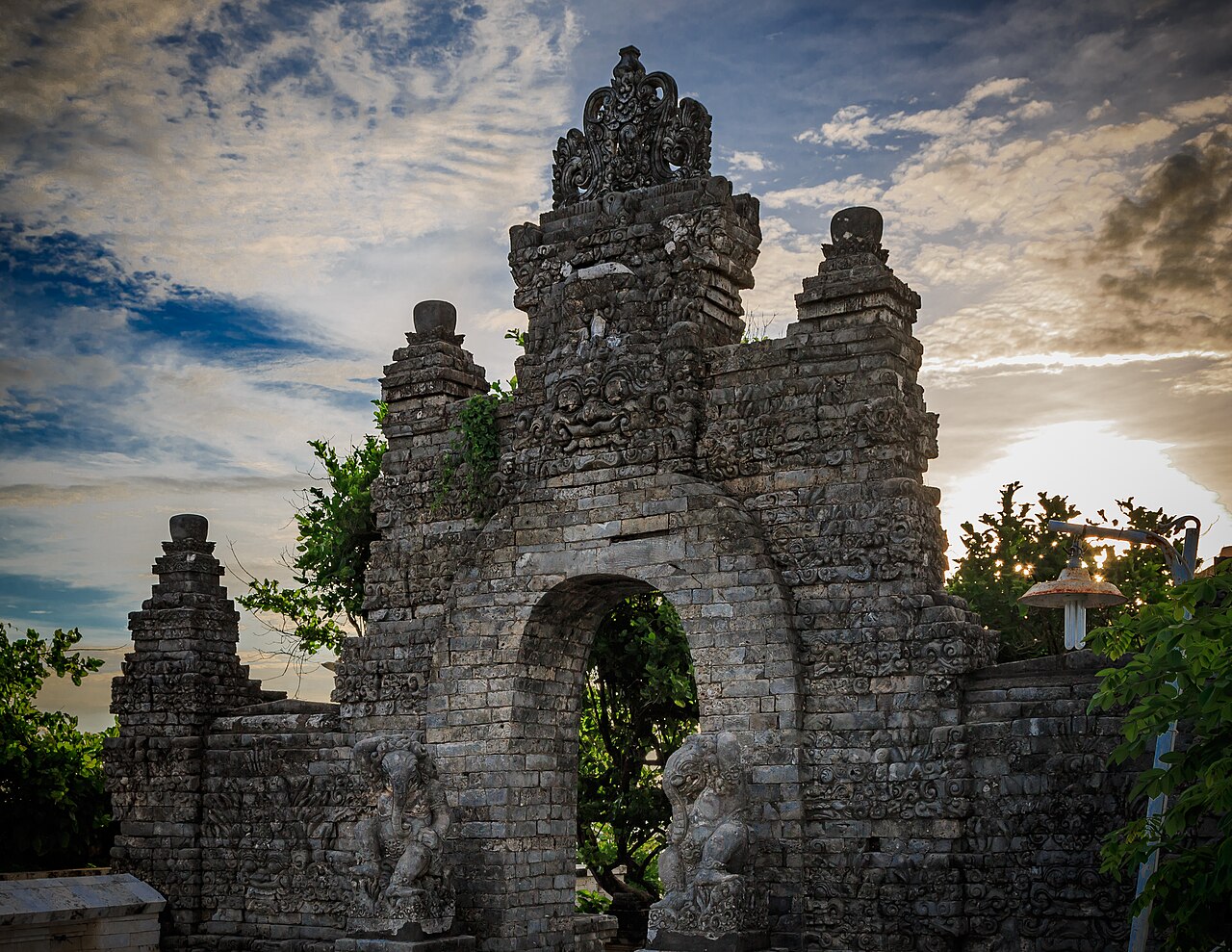 Verziertes graues Steintor mit Torbogen und Wächterfiguren am Tempel Pura Luhur Uluwatu im Abendlicht