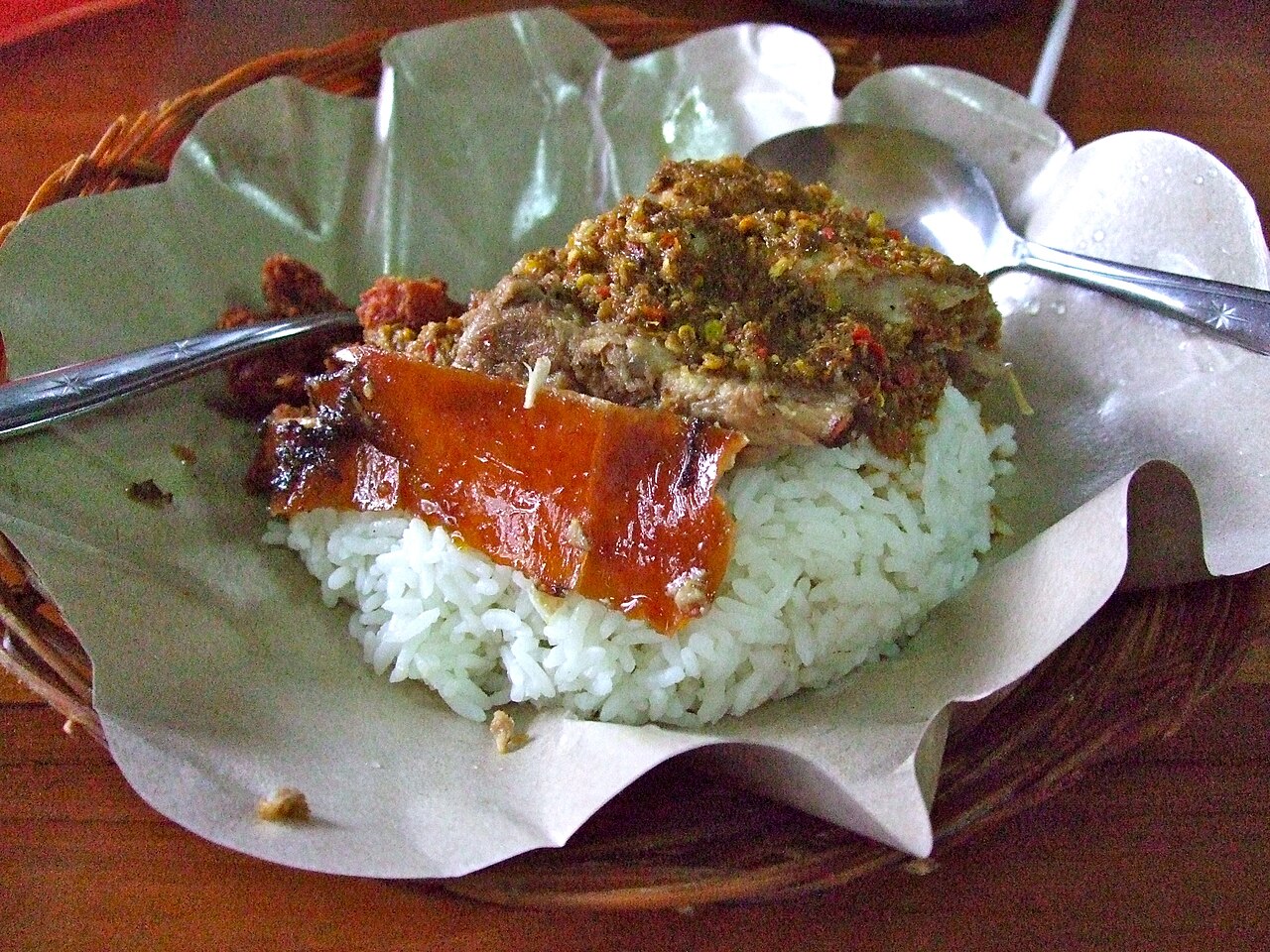 Portion Babi Guling mit knuspriger Schwarte, gewürztem Schweinefleisch und weißem Reis im Korbteller