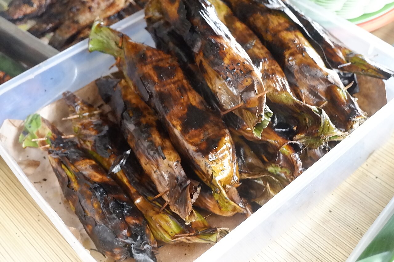 Mehrere angekohlte Bananenblattpäckchen mit Fisch, nebeneinander in einer weißen Schale
