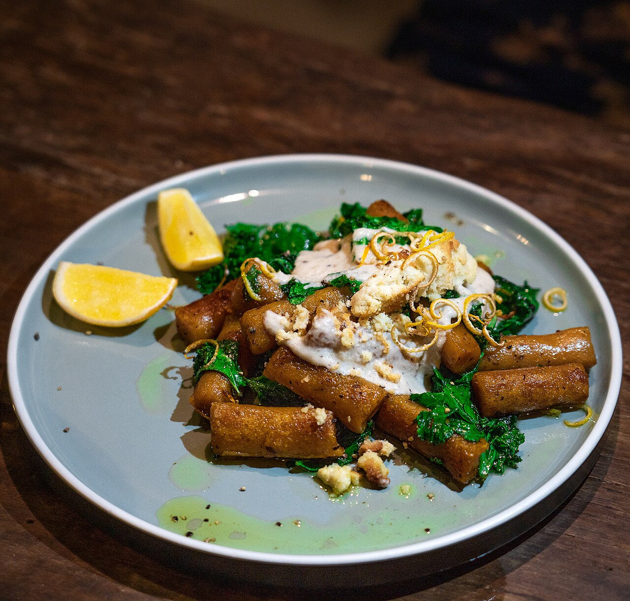 Teller mit gebratenen Süßkartoffel-Gnocchi, Grünkohl, heller Sauce, Nüssen und zwei Zitronenspalten