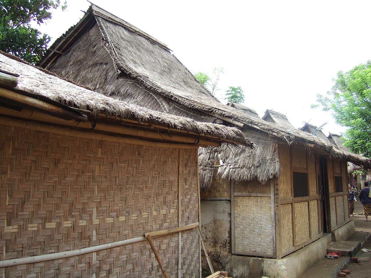 Traditionelle Sasak-Häuser mit Flechtwänden und Grasdächern an einem Weg im Dorf Sade auf Lombok
