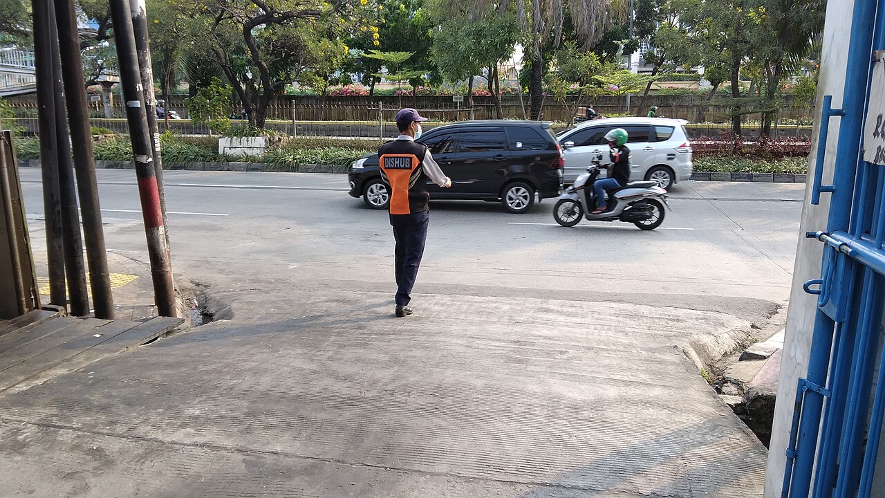 Verkehrshelfer mit orangefarbener Weste winkt in Jakarta ein Auto und einen Motorroller durch