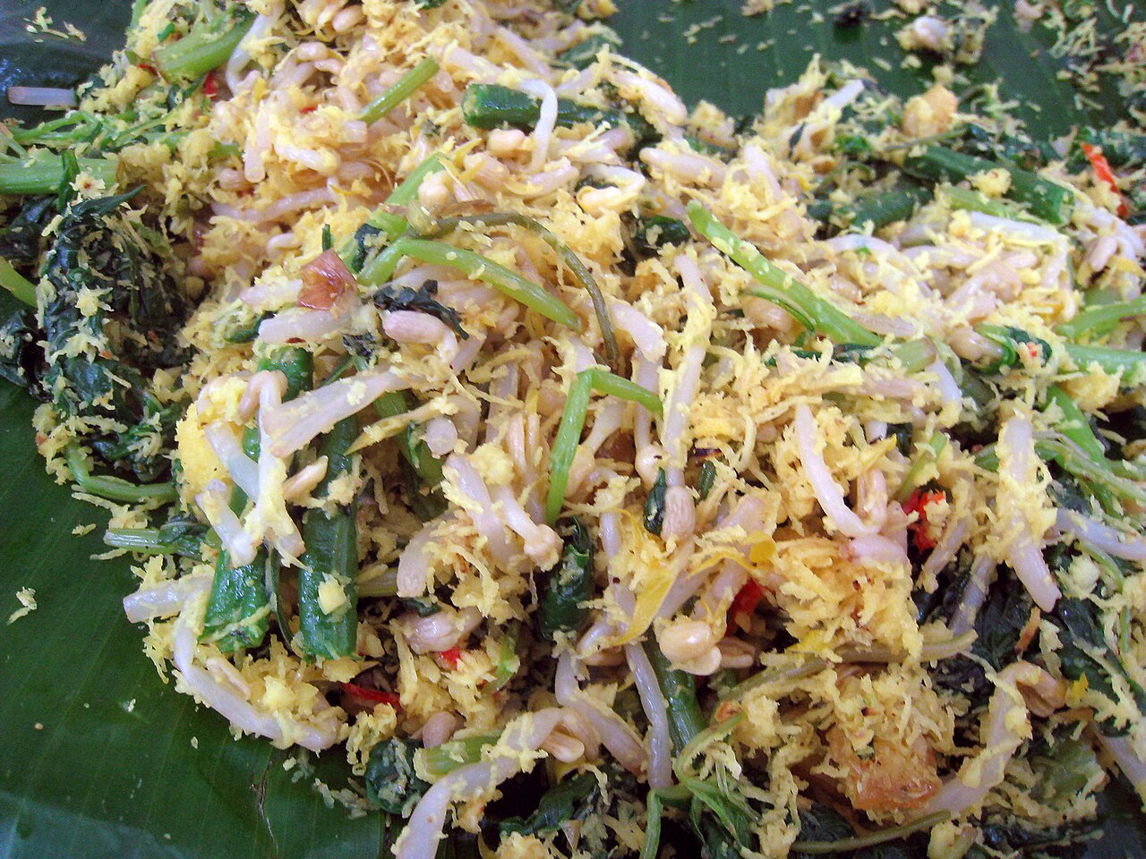 Nahaufnahme von Urap mit Sojasprossen, grünen Bohnen, Blattgemüse und gewürzten Kokosraspeln auf Bananenblatt